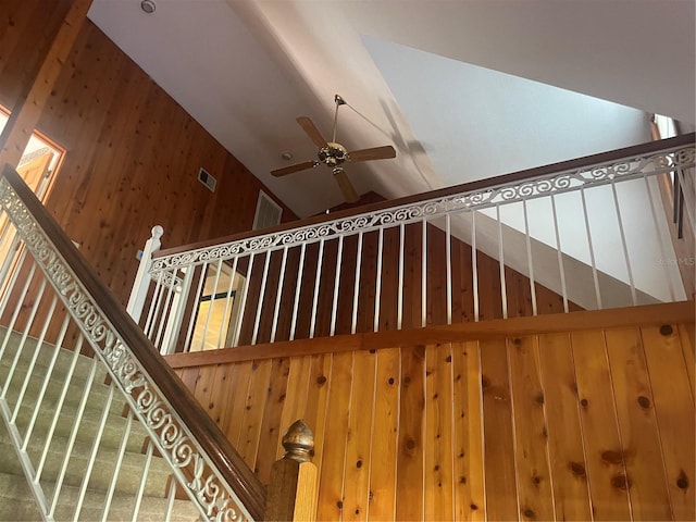 staircase with wood walls, high vaulted ceiling, and ceiling fan