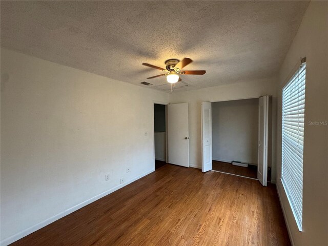 unfurnished bedroom featuring a textured ceiling, baseboard heating, a closet, wood-type flooring, and ceiling fan