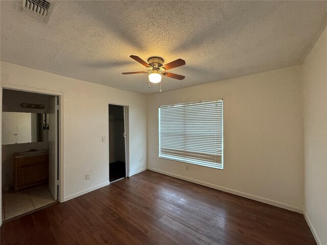 unfurnished bedroom featuring ensuite bathroom, a closet, dark wood-type flooring, ceiling fan, and a textured ceiling