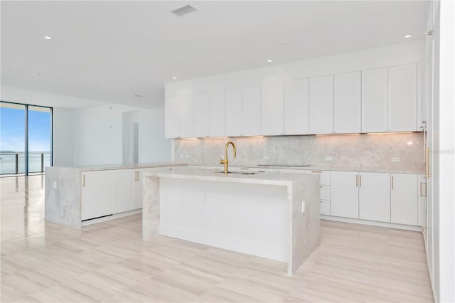 kitchen featuring an island with sink, sink, decorative backsplash, black electric stovetop, and white cabinets