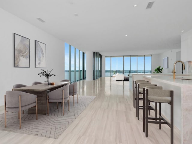 dining room featuring a water view, expansive windows, light hardwood / wood-style floors, and sink