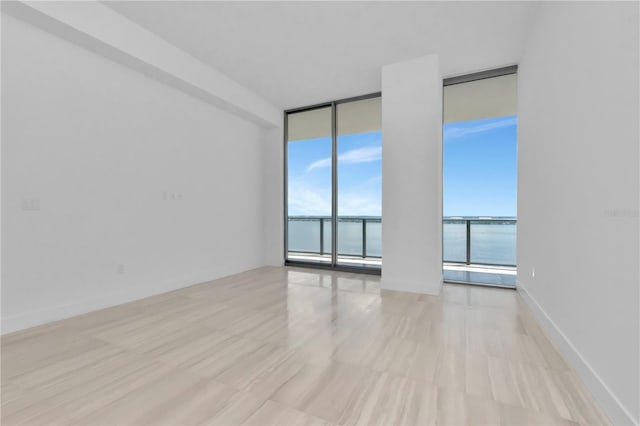 unfurnished room with light wood-type flooring, a water view, and expansive windows