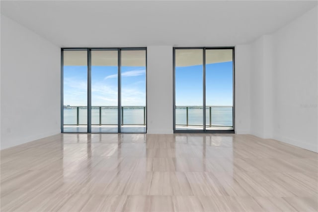 spare room featuring light hardwood / wood-style flooring, a water view, and floor to ceiling windows