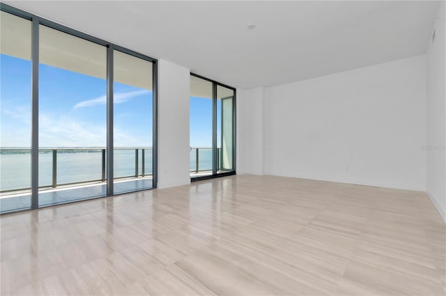 unfurnished room featuring light hardwood / wood-style floors, a water view, and a wall of windows