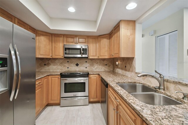 kitchen with sink, light stone countertops, appliances with stainless steel finishes, and a tray ceiling