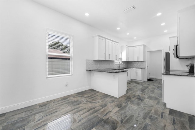 kitchen featuring dark stone counters, appliances with stainless steel finishes, kitchen peninsula, and white cabinets