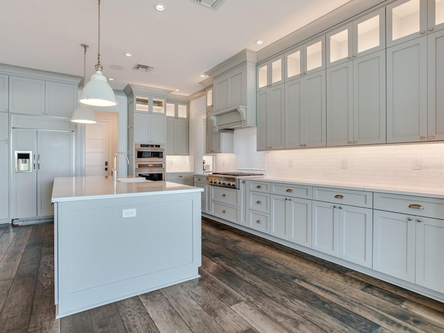 kitchen with hanging light fixtures, sink, a kitchen island with sink, appliances with stainless steel finishes, and dark hardwood / wood-style floors