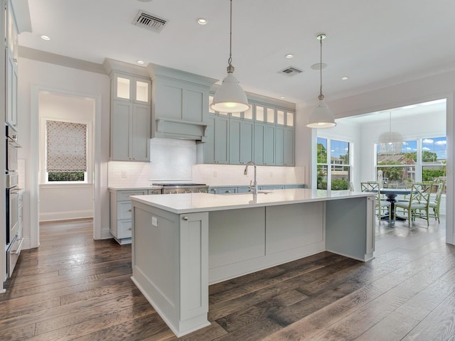 kitchen with pendant lighting, a kitchen island with sink, sink, backsplash, and dark hardwood / wood-style flooring