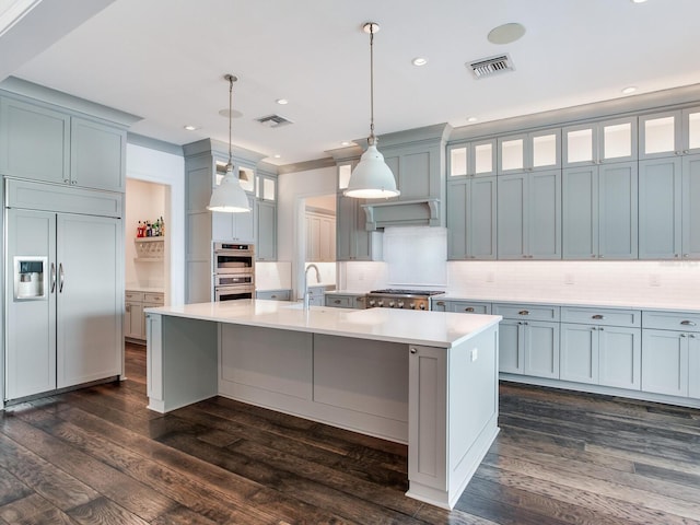 kitchen with hanging light fixtures, dark wood-type flooring, stainless steel appliances, a kitchen island with sink, and sink