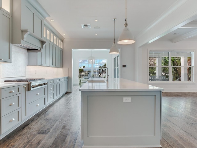 kitchen with hanging light fixtures, stainless steel gas cooktop, a center island with sink, gray cabinets, and hardwood / wood-style flooring