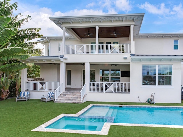 back of property featuring ceiling fan, a balcony, a lawn, and a swimming pool with hot tub