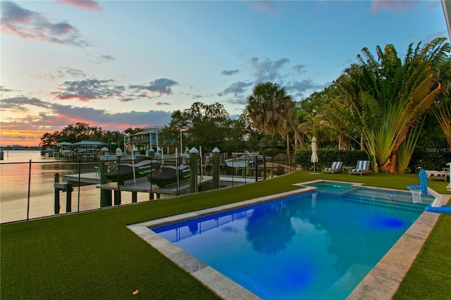 pool at dusk with a boat dock, a lawn, and a water view