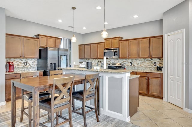 kitchen featuring pendant lighting, light tile patterned floors, appliances with stainless steel finishes, a kitchen island with sink, and light stone counters