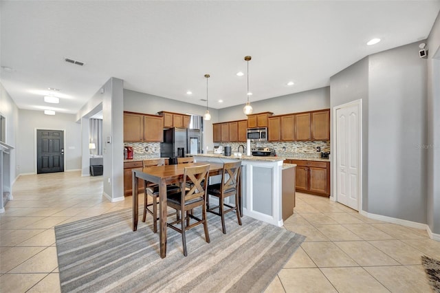 kitchen with an island with sink, stainless steel appliances, decorative light fixtures, and tasteful backsplash