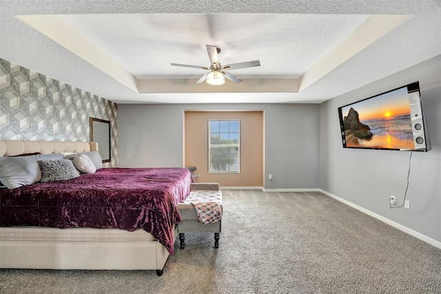 bedroom featuring a tray ceiling, a textured ceiling, ceiling fan, and carpet flooring