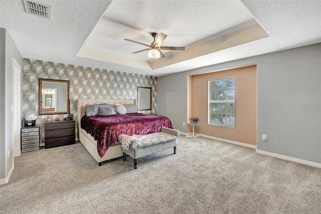 bedroom featuring a tray ceiling, light colored carpet, ceiling fan, and a textured ceiling