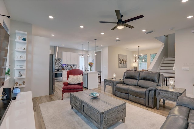 living room with light wood-type flooring, ceiling fan with notable chandelier, and sink