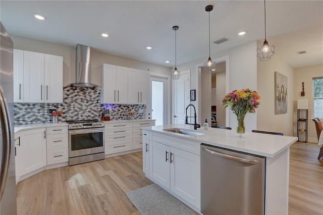 kitchen featuring white cabinetry, light hardwood / wood-style flooring, sink, appliances with stainless steel finishes, and wall chimney range hood