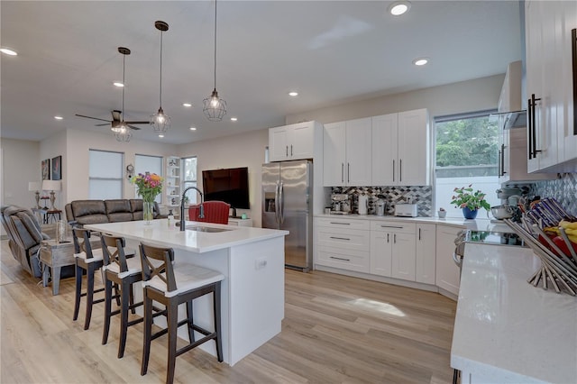 kitchen with stainless steel fridge with ice dispenser, a kitchen island with sink, hanging light fixtures, sink, and ceiling fan