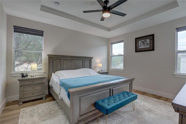 bedroom with ceiling fan, light wood-type flooring, and a tray ceiling