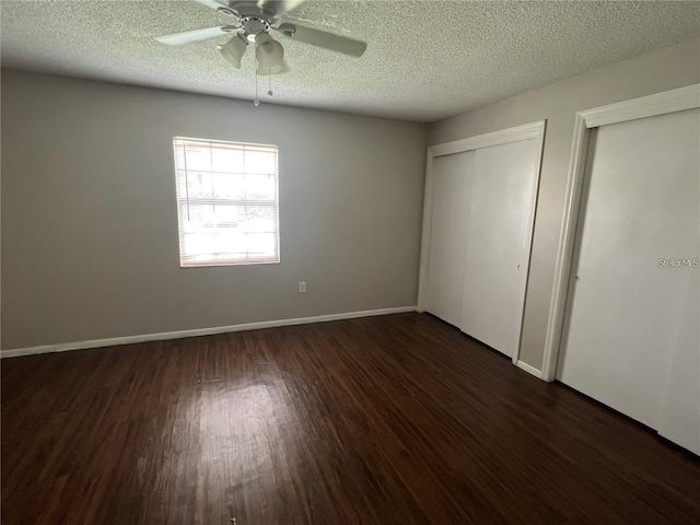 unfurnished bedroom with a textured ceiling, two closets, ceiling fan, and dark hardwood / wood-style floors