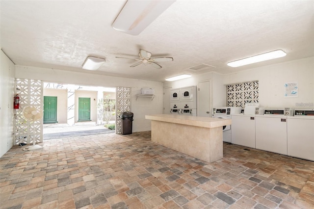 kitchen with light countertops, white cabinets, stacked washer / drying machine, a ceiling fan, and a center island