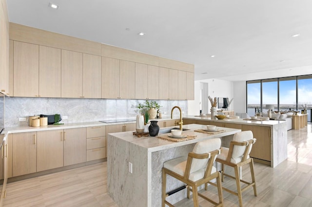 kitchen with light wood-type flooring, tasteful backsplash, light brown cabinetry, and an island with sink