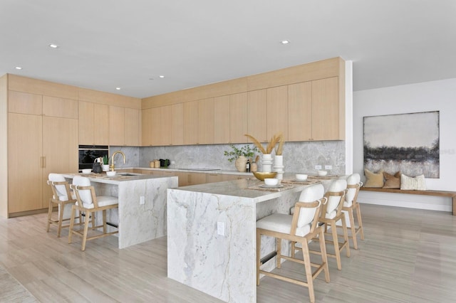 kitchen featuring light hardwood / wood-style flooring, light brown cabinetry, a kitchen island with sink, and a breakfast bar