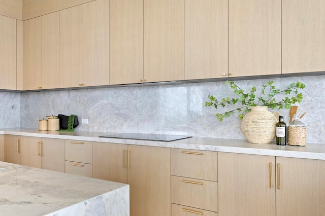 kitchen featuring light brown cabinetry, light stone counters, black electric cooktop, and tasteful backsplash