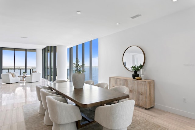 dining area featuring a water view, expansive windows, a healthy amount of sunlight, and light hardwood / wood-style floors