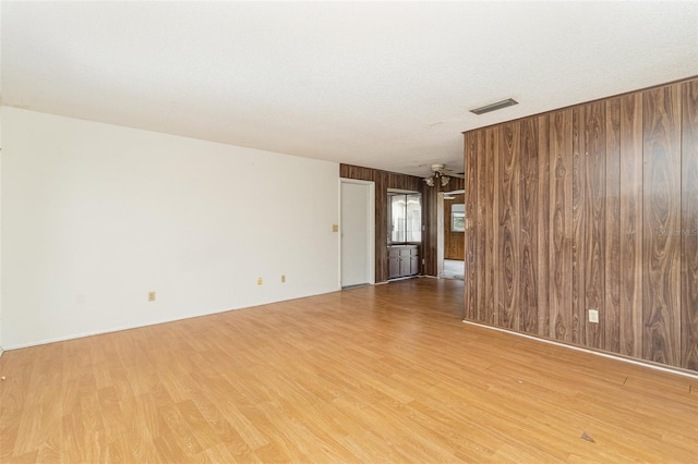 unfurnished room featuring a textured ceiling, light wood-type flooring, and wood walls