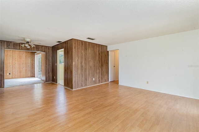 spare room featuring light wood-type flooring, a textured ceiling, and wooden walls