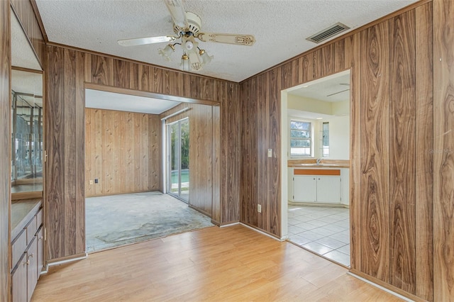 interior space featuring a textured ceiling, ceiling fan, sink, light hardwood / wood-style floors, and wood walls