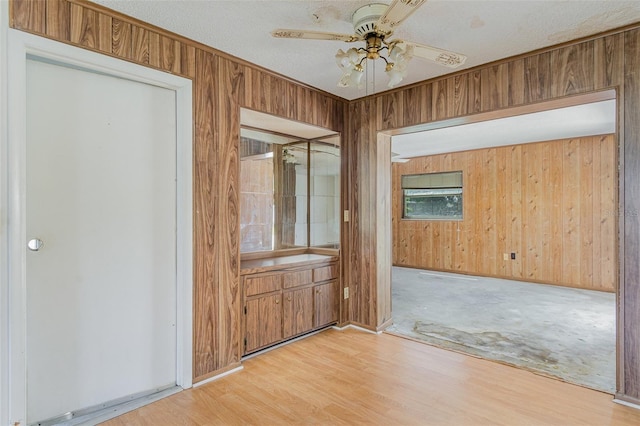 interior space with a textured ceiling, light hardwood / wood-style floors, ceiling fan, and wood walls