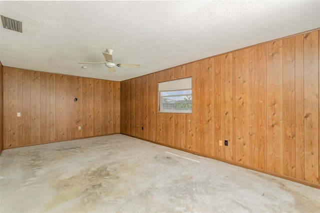 empty room with wood walls, ceiling fan, and a textured ceiling