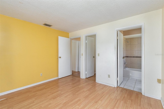 unfurnished bedroom featuring a textured ceiling, light hardwood / wood-style flooring, and ensuite bath