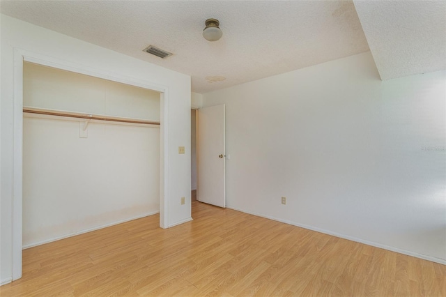 unfurnished bedroom with a textured ceiling, light wood-type flooring, and a closet