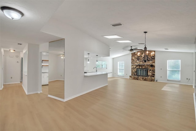 unfurnished living room featuring lofted ceiling with skylight, a fireplace, ceiling fan, and light hardwood / wood-style flooring