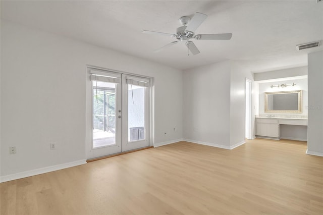 spare room featuring built in desk, light hardwood / wood-style floors, ceiling fan, and french doors