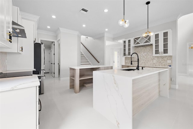 kitchen with ventilation hood, stainless steel fridge, pendant lighting, white cabinets, and a kitchen island with sink