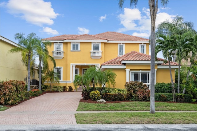 mediterranean / spanish-style house with a balcony, a tile roof, decorative driveway, a front lawn, and stucco siding