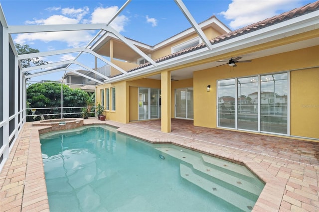 view of swimming pool featuring glass enclosure, a pool with connected hot tub, a patio area, and a ceiling fan