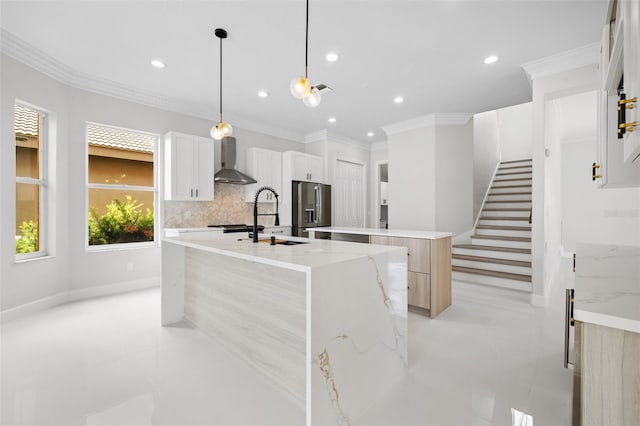 kitchen featuring stainless steel fridge with ice dispenser, a kitchen island with sink, wall chimney range hood, a sink, and backsplash