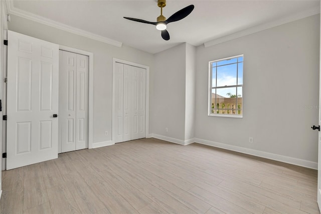 unfurnished bedroom featuring multiple closets, baseboards, light wood-style flooring, ornamental molding, and ceiling fan