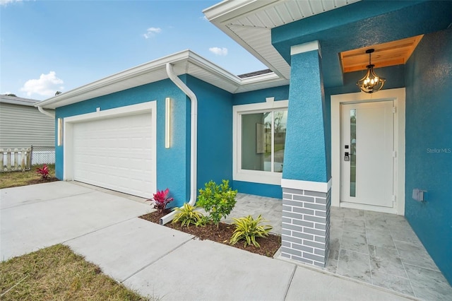 doorway to property with an attached garage, driveway, fence, and stucco siding