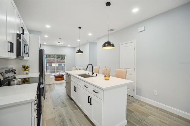 kitchen with appliances with stainless steel finishes, wood tiled floor, white cabinets, and a sink