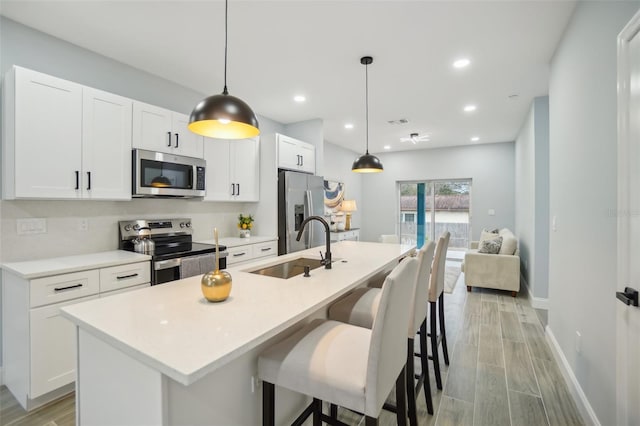 kitchen featuring stainless steel appliances, wood tiled floor, white cabinets, a kitchen island with sink, and a sink