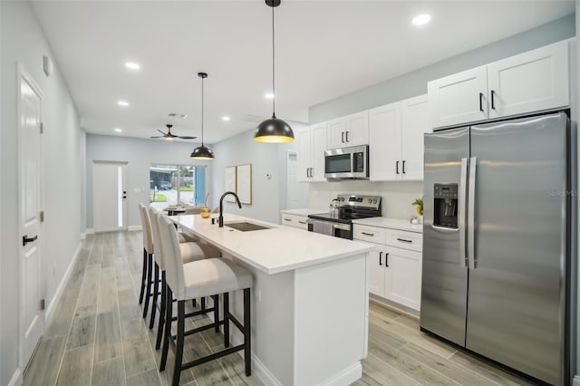 kitchen with wood finish floors, a sink, white cabinetry, appliances with stainless steel finishes, and an island with sink