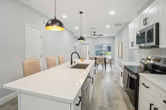 kitchen featuring light wood-style flooring, a sink, white cabinetry, appliances with stainless steel finishes, and an island with sink