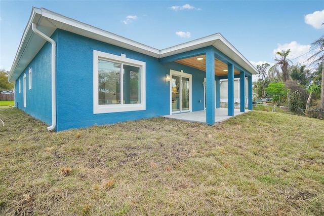 back of house with a patio, a lawn, and stucco siding